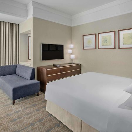 Jabal Omar Hyatt Regency Makkah Hotel Mecca Exterior photo The photo shows a modern hotel room featuring a neatly made bed with white linens, a small blue couch to the side, and a wooden dresser with a television mounted on the wall above it. There are two framed pieces of art on the wall near the bed, and t