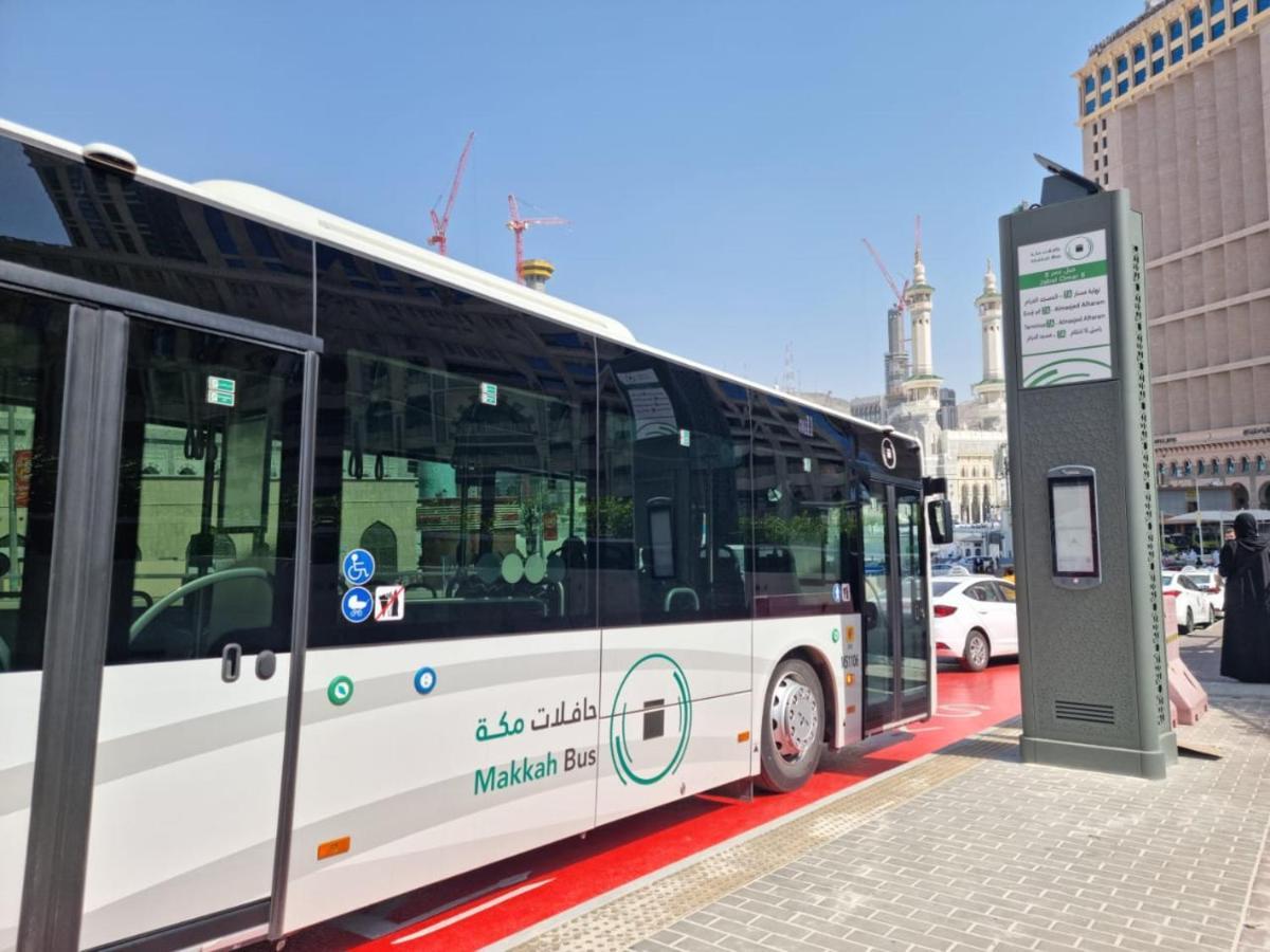 Jabal Omar Hyatt Regency Makkah Hotel Mecca Exterior photo The photo shows a public bus labeled "Makkah Bus," parked at a designated bus stop. The bus has a modern design and is predominantly white, with green accents. In the background, there are tall buildings and construction cranes, indicating a busy urb