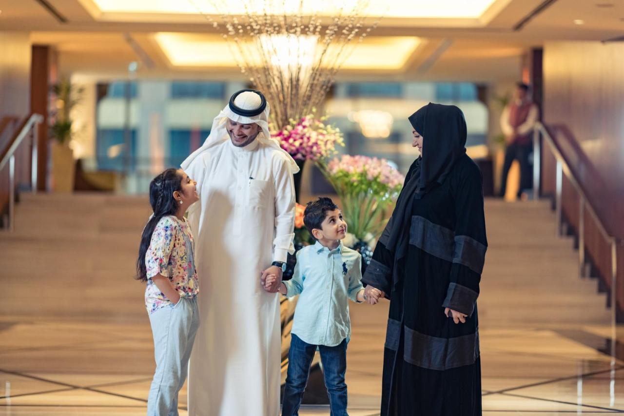 Jabal Omar Hyatt Regency Makkah Hotel Mecca Exterior photo The photo shows a family in a hotel lobby. There are two children, a boy and a girl, standing between their parents. The girl is smiling and looking up at her father, who is wearing traditional white attire and a headscarf. The boy is also smiling an