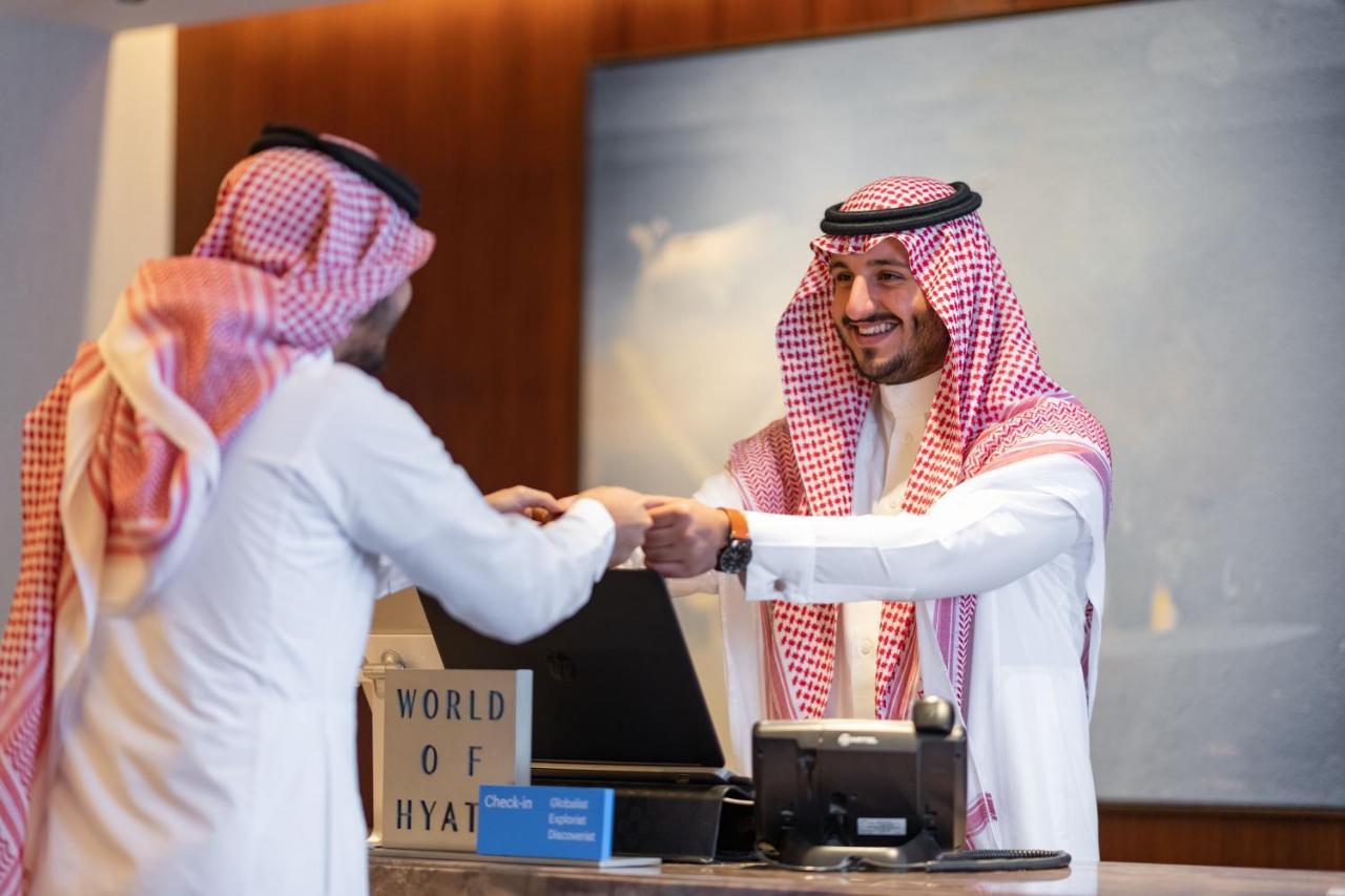 Jabal Omar Hyatt Regency Makkah Hotel Mecca Exterior photo The photo shows a scene at a hotel reception desk. A hotel staff member, dressed in traditional attire, is smiling and handing something to a guest, who is also wearing traditional clothing. The guest appears to be receiving a key or a document. The 