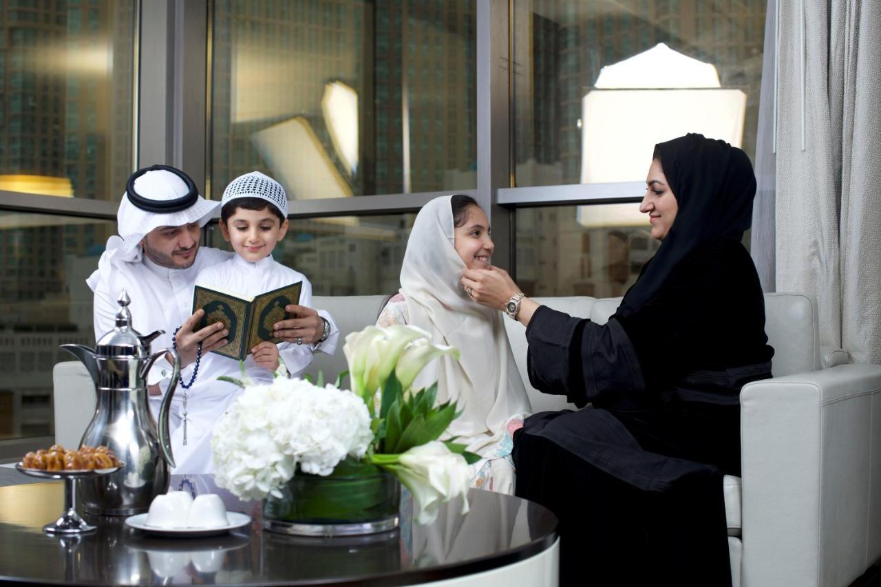 Jabal Omar Hyatt Regency Makkah Hotel Mecca Exterior photo The photo depicts a family gathering in a modern, well-furnished setting. A man and a boy, both dressed in traditional attire, are engaged in reading from a book, likely the Quran. A woman, wearing a hijab and a black abaya, is sitting next to them, 