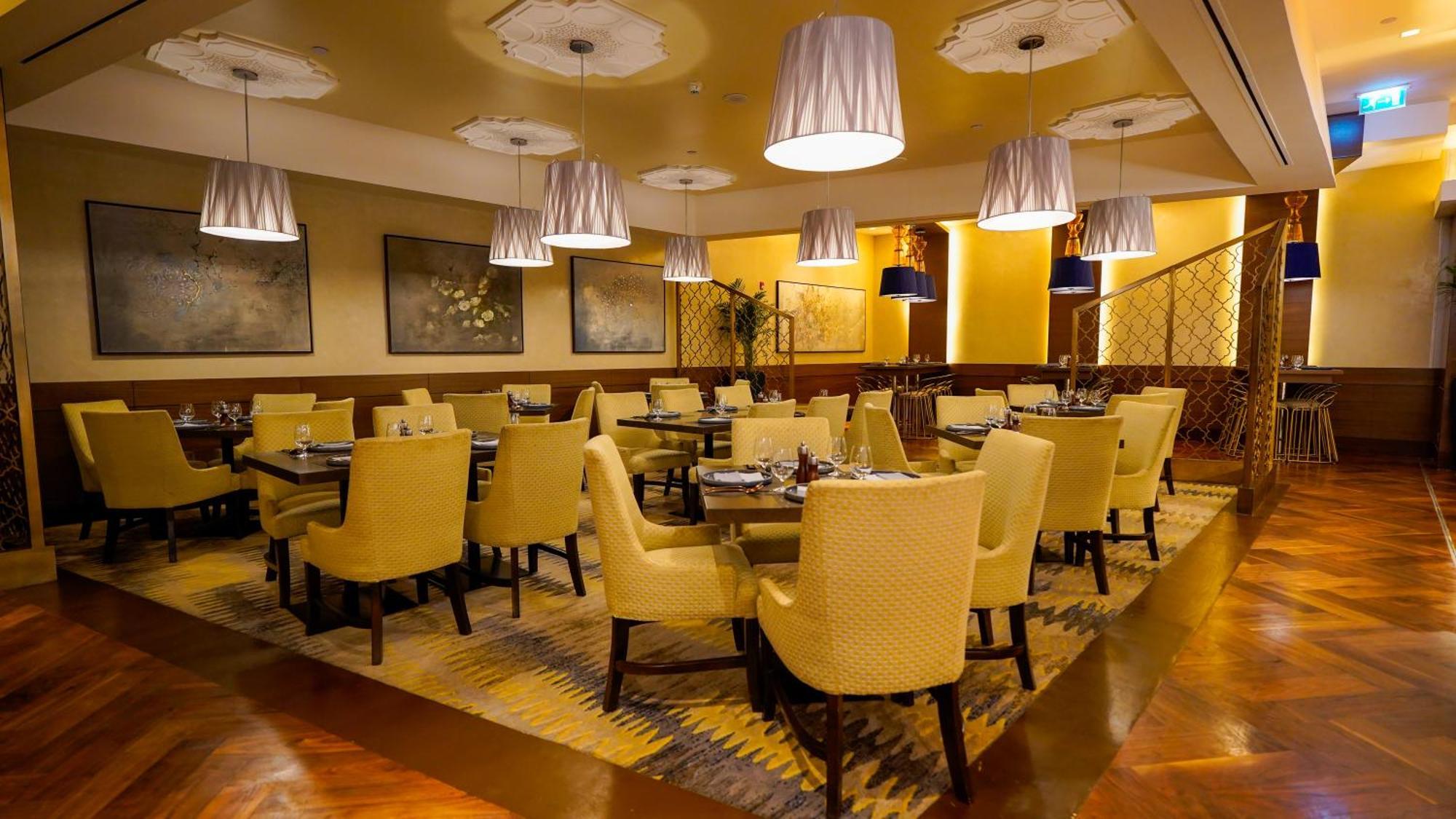 Jabal Omar Hyatt Regency Makkah Hotel Mecca Exterior photo The photo shows an elegant restaurant interior. There are several tables arranged with yellow upholstered chairs, creating a warm and inviting atmosphere. Soft lighting is provided by modern pendant lamps hanging from the ceiling. The floor features 