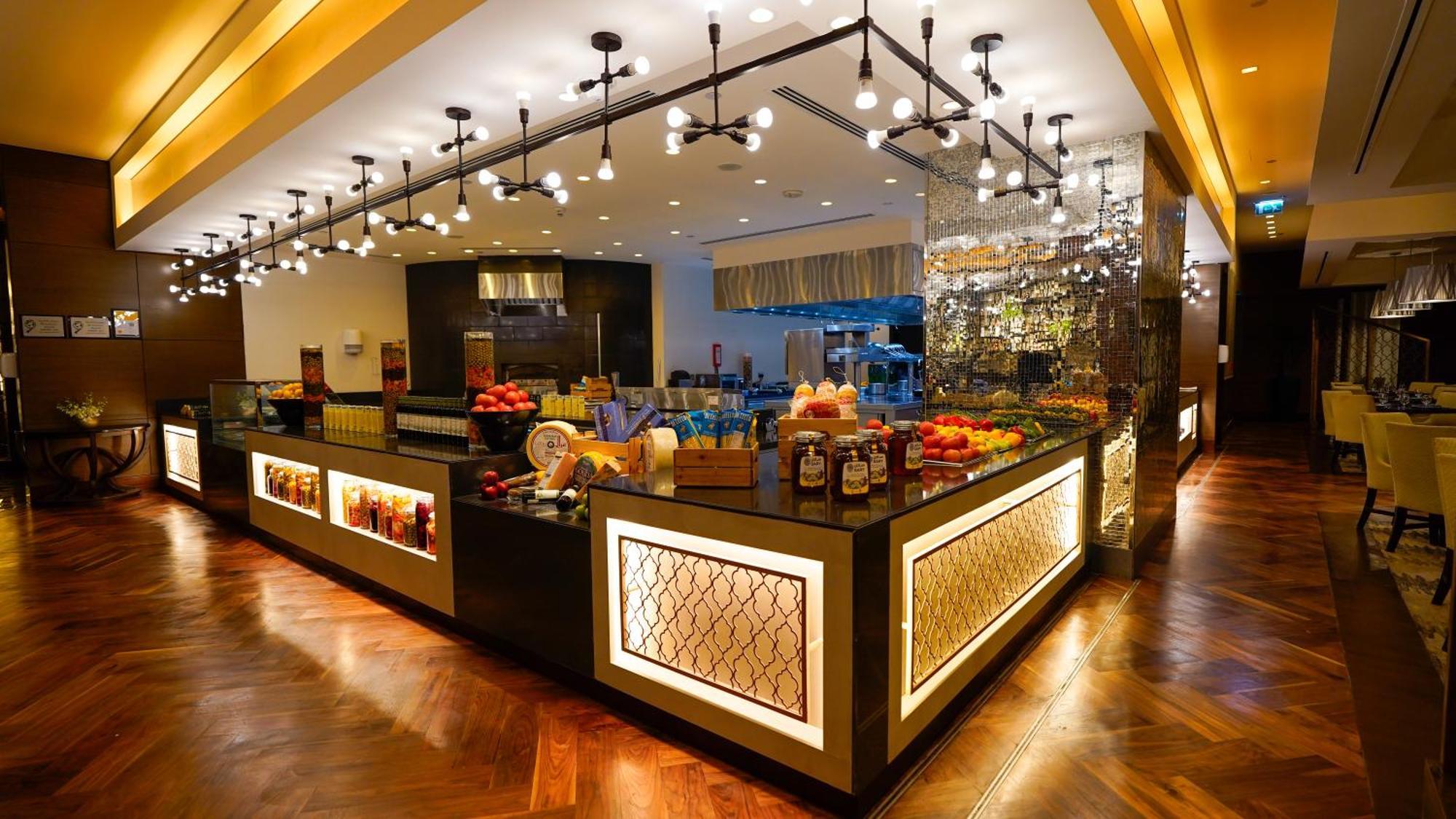 Jabal Omar Hyatt Regency Makkah Hotel Mecca Exterior photo The photo shows a stylish and modern buffet area in a restaurant or hotel. The design features a sleek counter with various food items displayed, including fresh fruits. The space is well-lit with pendant lights hanging from the ceiling, creating a w