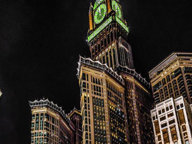 Jabal Omar Hyatt Regency Makkah Hotel Mecca Exterior photo The photo shows a tall building, which is a prominent feature of a city skyline, illuminated against a dark night sky. At the top of the building is a large clock tower, noticeable for its distinct green color, and intricate architectural details. Th