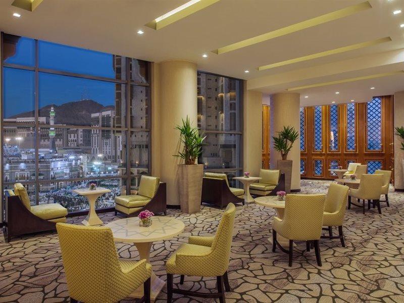 Jabal Omar Hyatt Regency Makkah Hotel Mecca Exterior photo The photo shows a modern, well-lit lounge or reception area. It features several small round tables surrounded by comfortable chairs, all in a soft yellow upholstery. The flooring is composed of stone tiles, adding a natural element to the decor. Lar