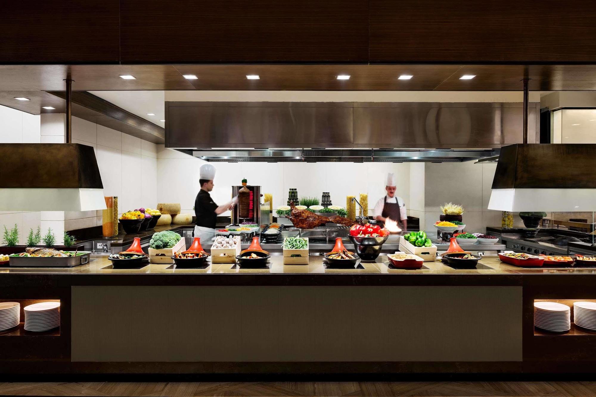 Jabal Omar Hyatt Regency Makkah Hotel Mecca Exterior photo The photo shows a well-organized kitchen or buffet area. In the foreground, there are several food stations displaying a variety of dishes, including fresh vegetables, meats, and other culinary items arranged in bowls or trays. Behind the counter, tw