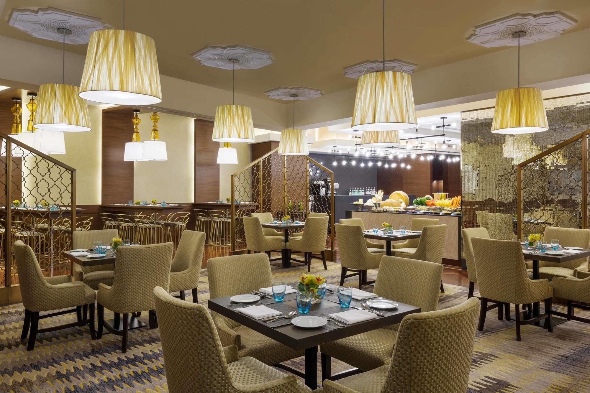 Jabal Omar Hyatt Regency Makkah Hotel Mecca Exterior photo The photo displays a modern restaurant interior. It features a series of round tables with beige upholstered chairs arranged neatly throughout the space. Each table is set with plates and blue-tinted glasses. The lighting is provided by stylish penda