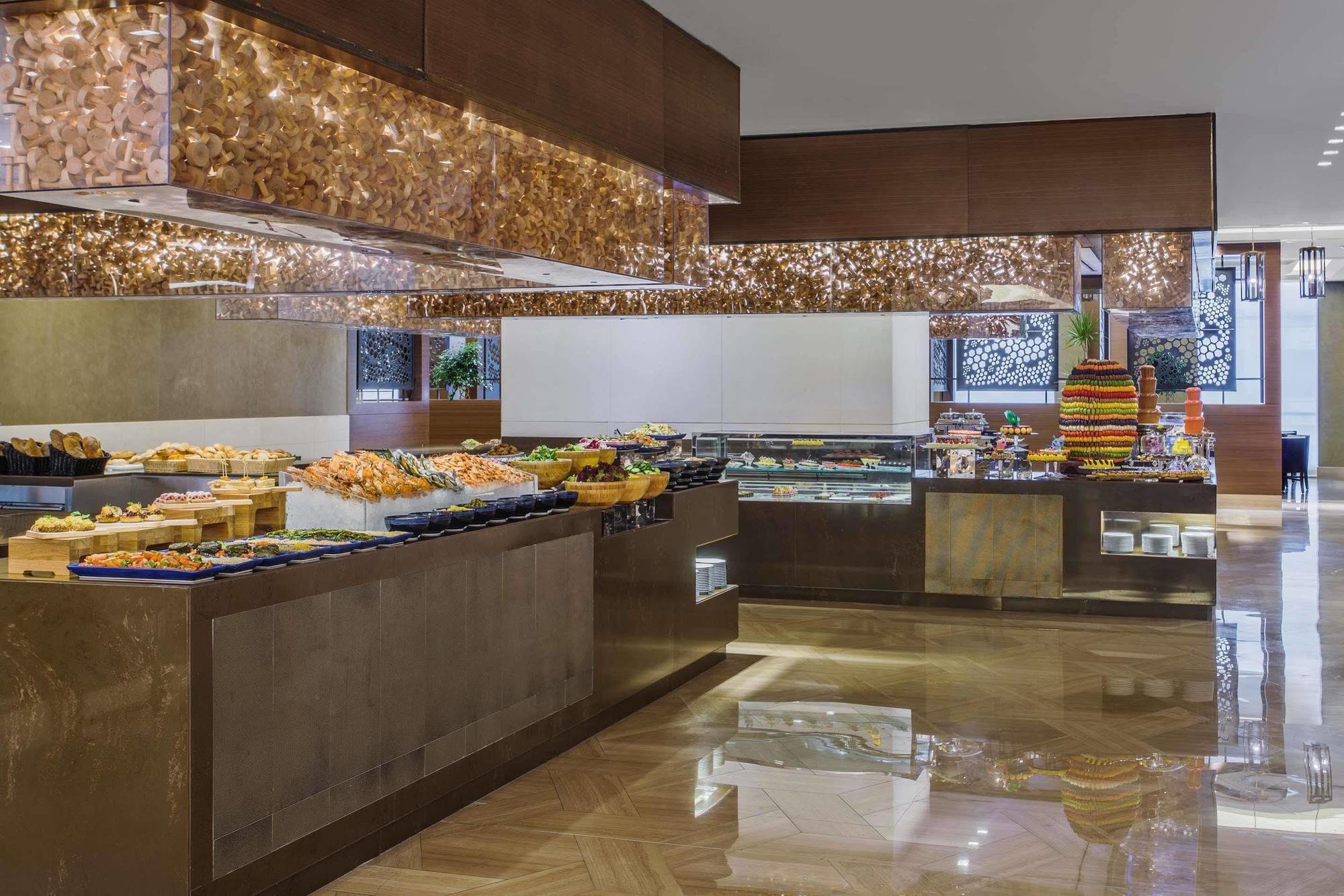 Jabal Omar Hyatt Regency Makkah Hotel Mecca Exterior photo The photo shows an elegant buffet setup in a spacious dining area. There are various food displays arranged on sleek surfaces, including an assortment of items such as pastries, fruits, and possibly other dishes. The decor features warm lighting with