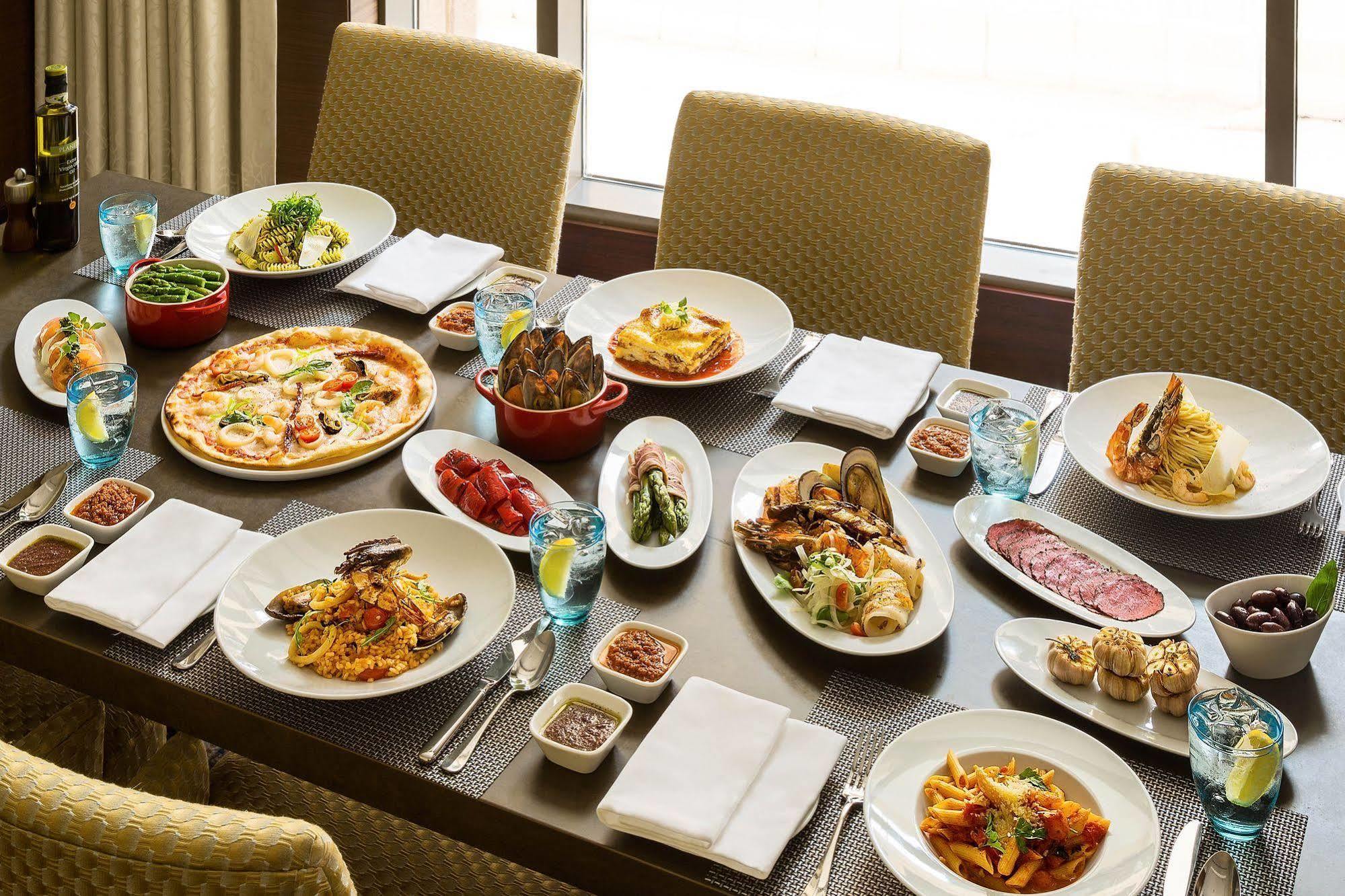 Jabal Omar Hyatt Regency Makkah Hotel Mecca Exterior photo The photo shows a large dining table set with various dishes, suggesting a festive or communal meal. There are several plates of food including:

- A pizza topped with vegetables and possibly meats.
- A serving of lasagna.
- A variety of pasta dishes