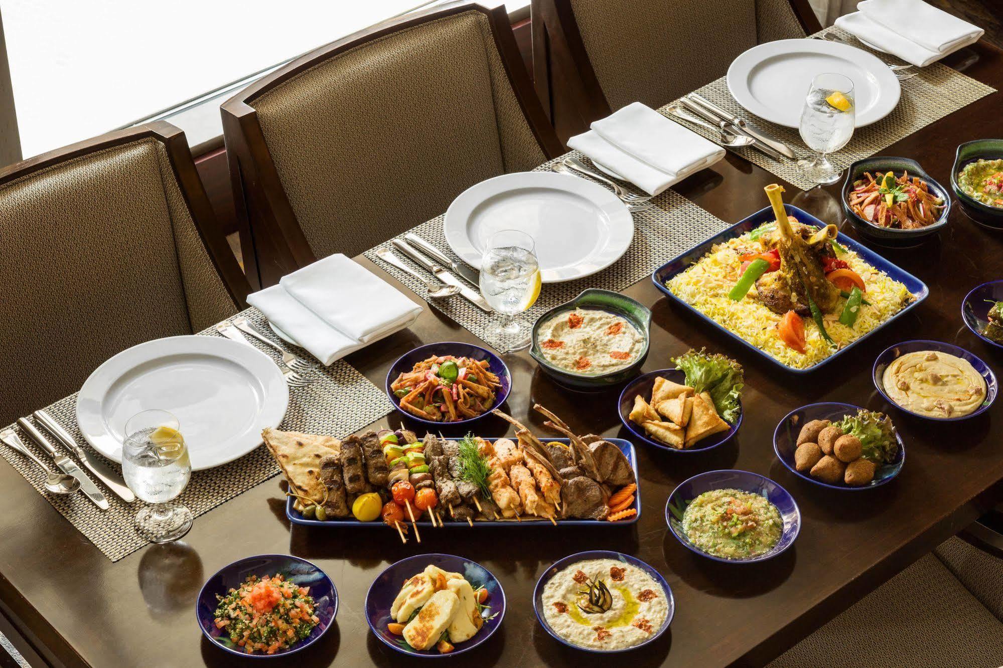 Jabal Omar Hyatt Regency Makkah Hotel Mecca Exterior photo The photo shows a beautifully arranged dining table set for a feast. There are several plates and dishes filled with a variety of foods:

1. **Main Dishes**: A large platter features grilled meats, including skewers and seasoned chicken, garnished wi