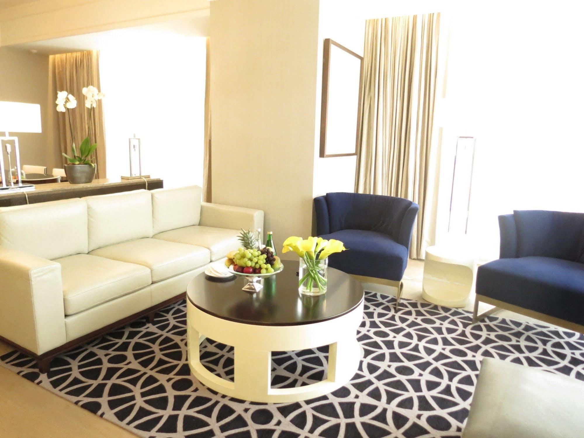 Jabal Omar Hyatt Regency Makkah Hotel Mecca Exterior photo The photo shows a stylish and modern living area. It features a white sectional sofa, two blue upholstered chairs, and a round black coffee table with a decorative centerpiece that includes flowers and fruits. The flooring is covered with a patterned