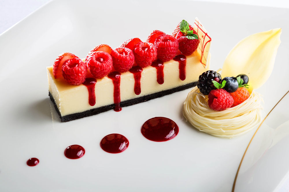 Jabal Omar Hyatt Regency Makkah Hotel Mecca Exterior photo The photo shows an elegantly plated dessert featuring a rectangular piece of cheesecake topped with fresh raspberries. The cheesecake is set on a dark crust, possibly made of chocolate or cookie crumbs. There are red fruit coulis drizzled artfully ar