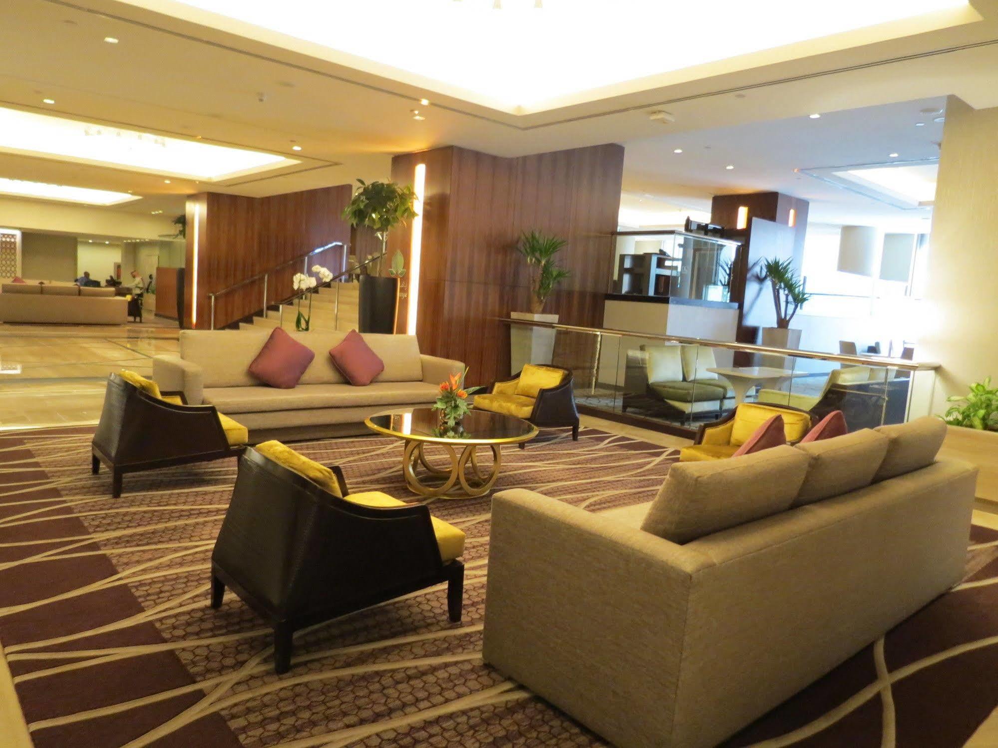 Jabal Omar Hyatt Regency Makkah Hotel Mecca Exterior photo The photo shows a modern and stylish lobby or lounge area. It features two large sofas with a light color and several cushions in shades of purple. There are also two armchairs with a darker finish and yellow cushions. In the center, there is a round