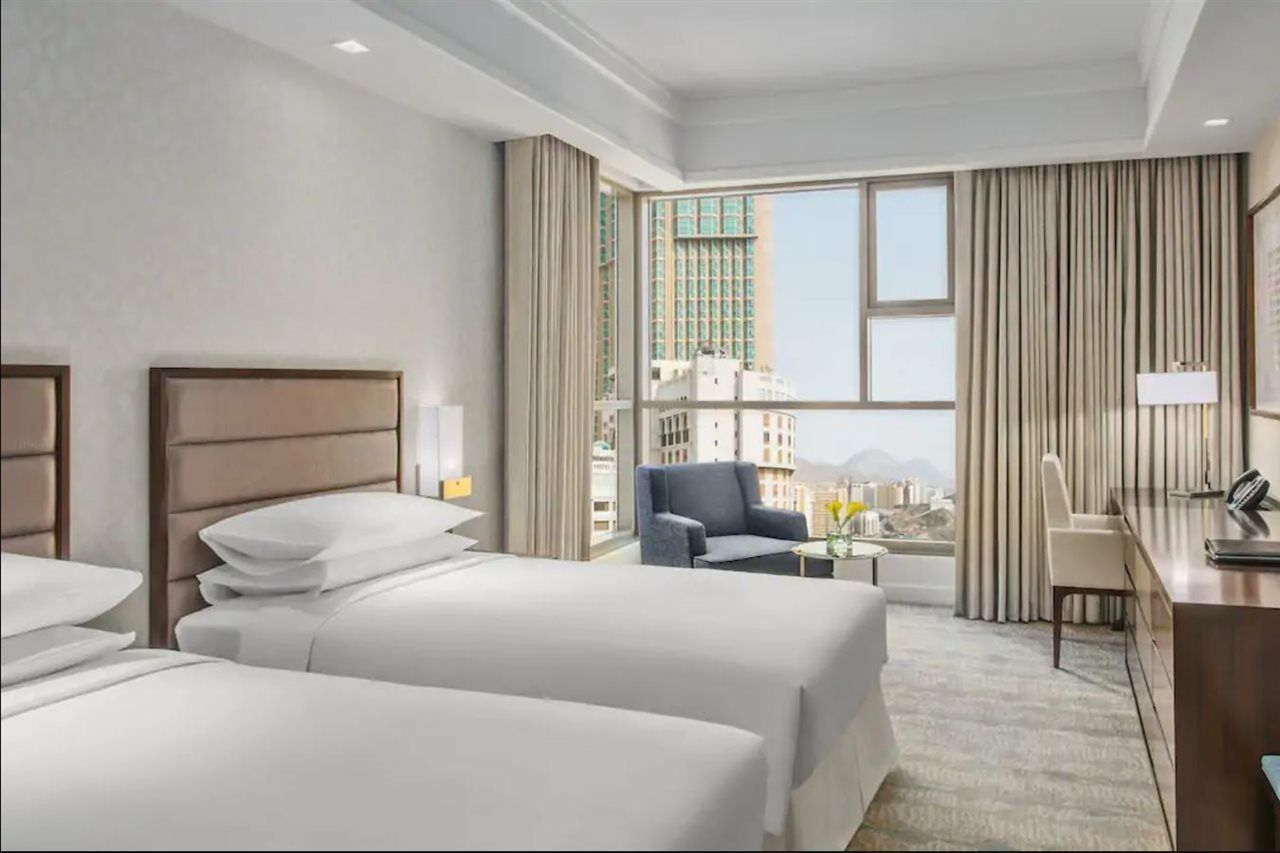 Jabal Omar Hyatt Regency Makkah Hotel Mecca Exterior photo The photo shows a modern hotel room featuring two beds with white linens. The room has a bright and airy feel, thanks to large windows that allow natural light to flood in. There are floor-to-ceiling curtains, and a small seating area with a chair an