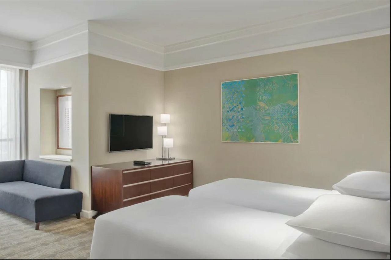 Jabal Omar Hyatt Regency Makkah Hotel Mecca Exterior photo The photo shows a hotel room featuring two twin beds with white bedding. A dark wooden dresser is positioned against one wall, with a flat-screen TV mounted above it. Next to the dresser, there are two modern lamps providing soft lighting. On the wal